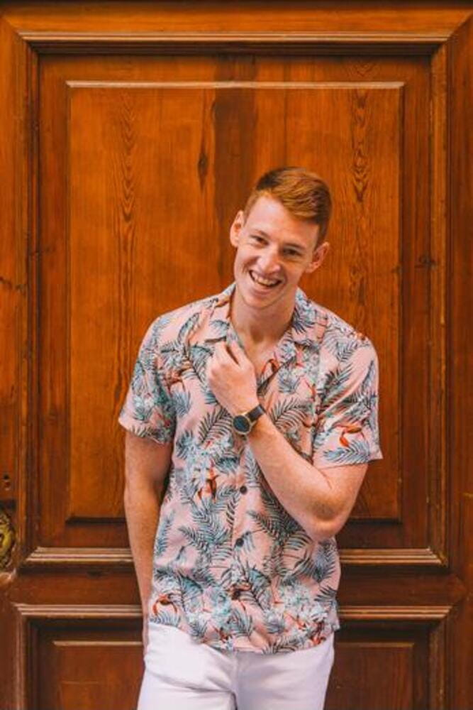 Handsome happy man male in hawaiian shirt leaning on wooden door looking at camera smiling Handsome happy man male in hawaiian shirt leaning on wooden door looking at camera smiling