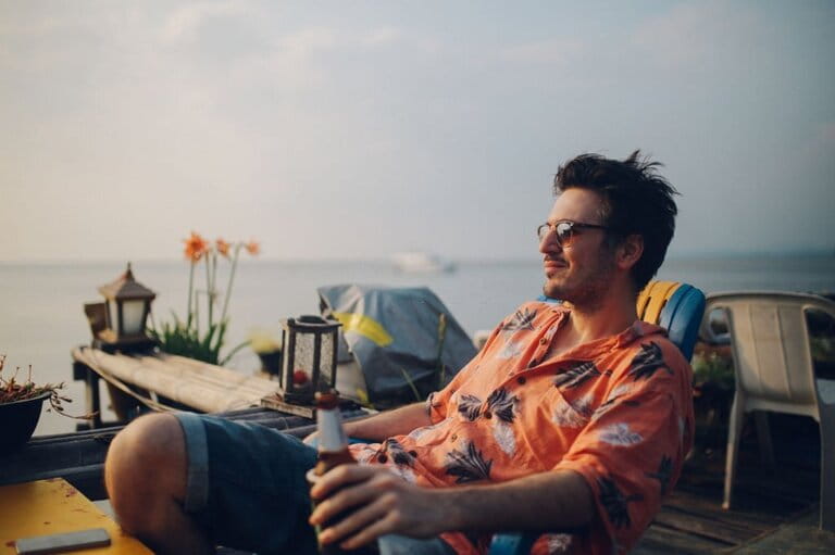 Young man relaxing by the beach, drinking beer, watching the sunset in Koh Lanta, Thailand Young man relaxing by the beach, drinking beer, watching the sunset in Koh Lanta, Thailand